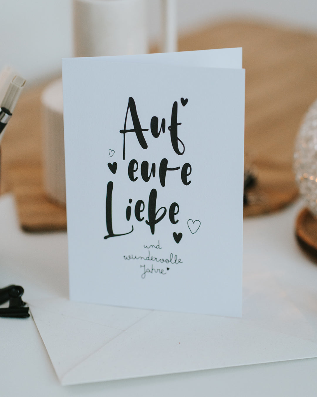 Hochzeitskarte „Auf eure Liebe“ aufgestellt vor passendem Umschlag, zeitloses Schwarz-Weiß-Design.