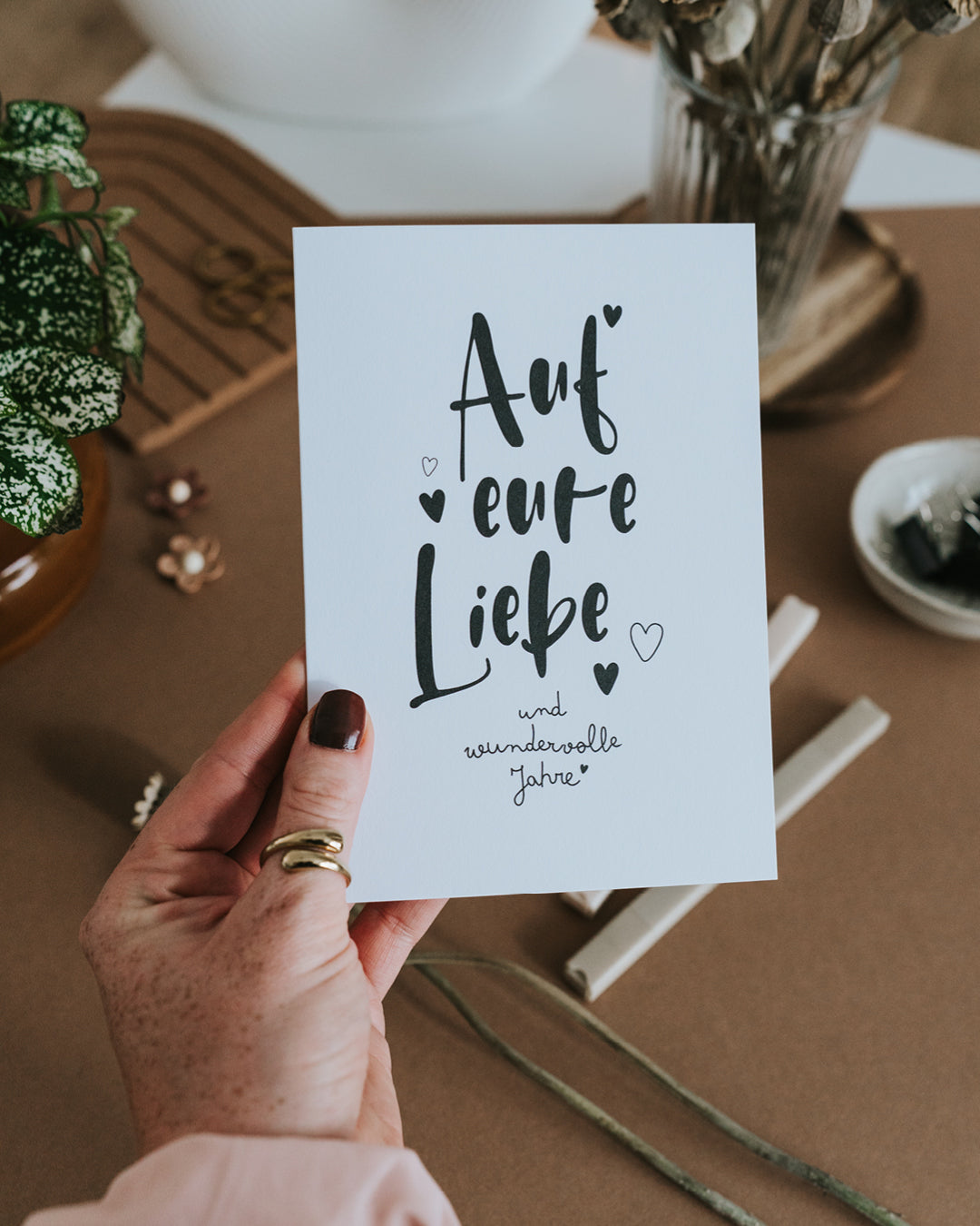 Hand hält Klappkarte „Auf eure Liebe“ – hochwertiges Papier im Hochformat mit Herz-Details.