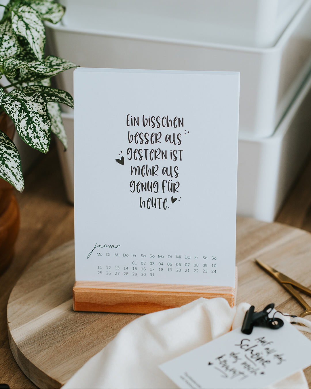Tischkalender 2027 im Holzständer mit Januar-Karte auf einem Holztisch.