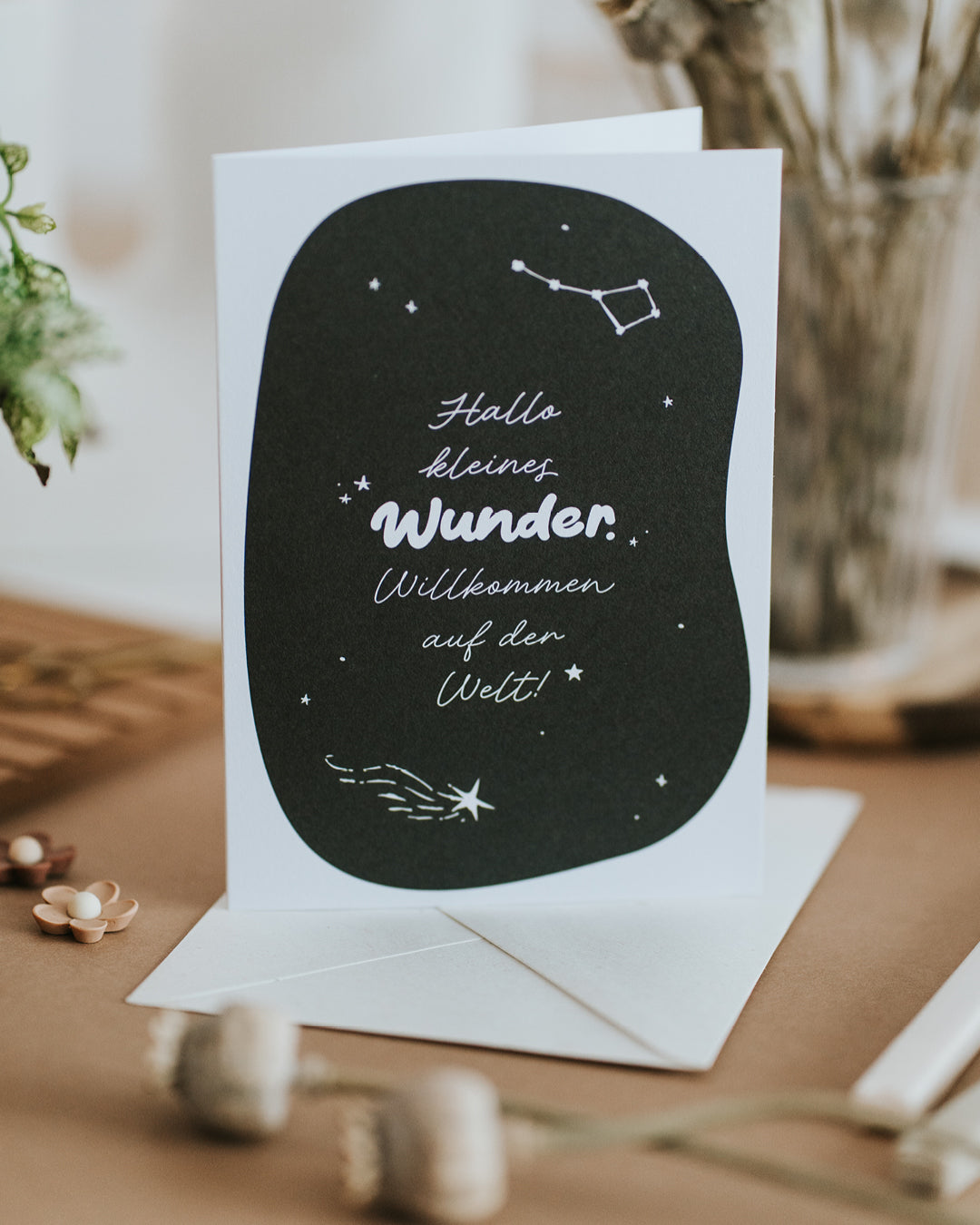 Geburtskarte mit Sternschnuppe und Handlettering, aufgestellt vor passendem Umschlag.