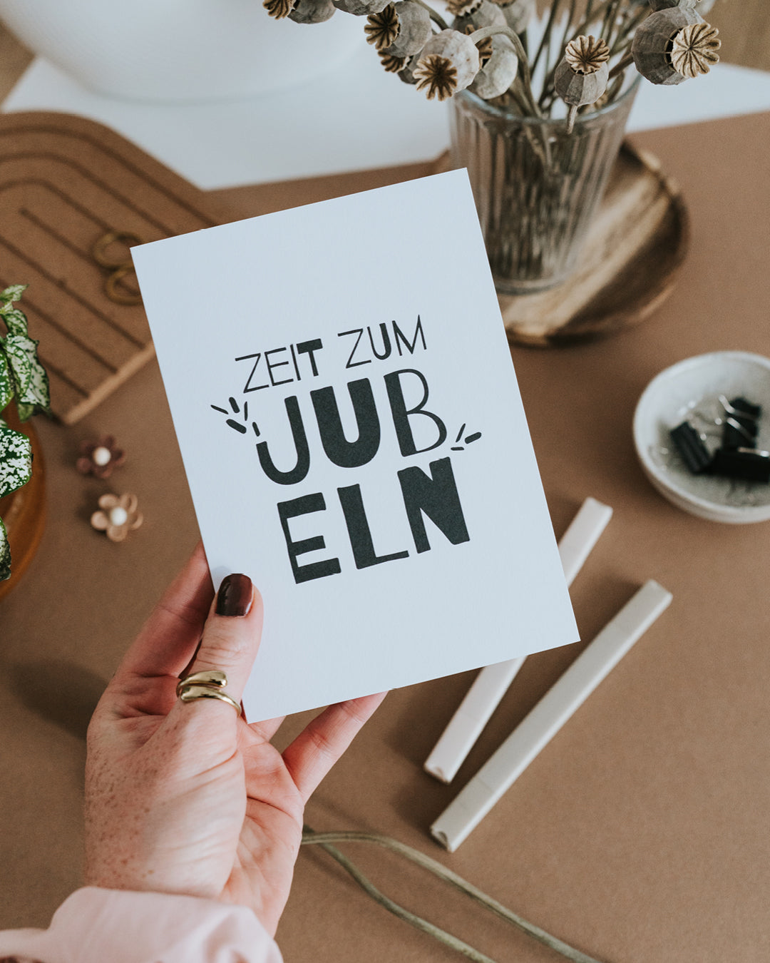 Hand hält Glückwunschkarte „Zeit zum Jubeln“ mit markantem Handlettering.