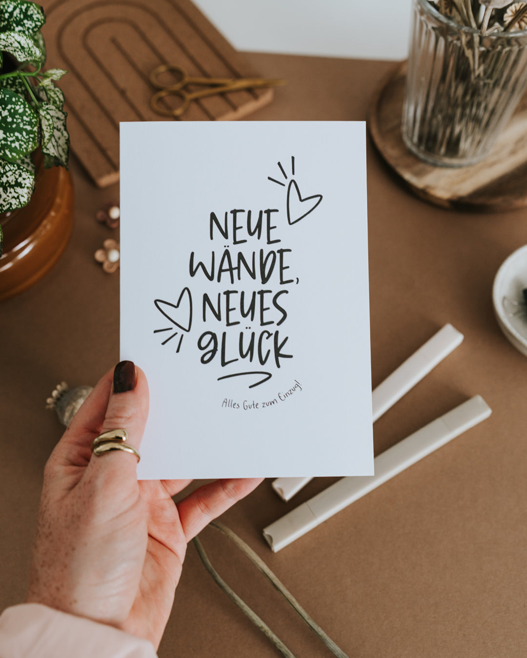 Hand hält Einzugskarte „Neue Wände, neues Glück – Alles Gute zum Einzug“ auf gutem Papier.